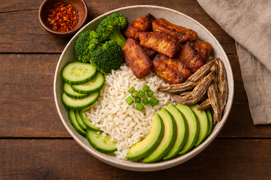close-up photograph of a nourishing dry fish bowl served in a ceramic bowl on a rustic wooden table, featuring fluffy white rice topped with crispy dry fish, pan-fried anchovies, sliced avocado, cucumber, steamed broccoli