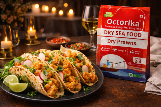 Indo-Mexican dry prawn tacos filled with spicy Indian masala, fresh herbs, radish slices, and lime wedges, served on a black plate beside an Octorika Dry Prawns packet