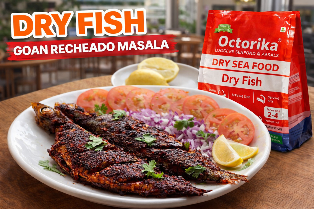 Goan-style dry fish coated in spicy red Recheado masala served on a white plate with sliced tomatoes, onions, lemon wedges, and fresh coriander, placed on a restaurant-style wooden table beside an Octorika Dry Fish packet.
