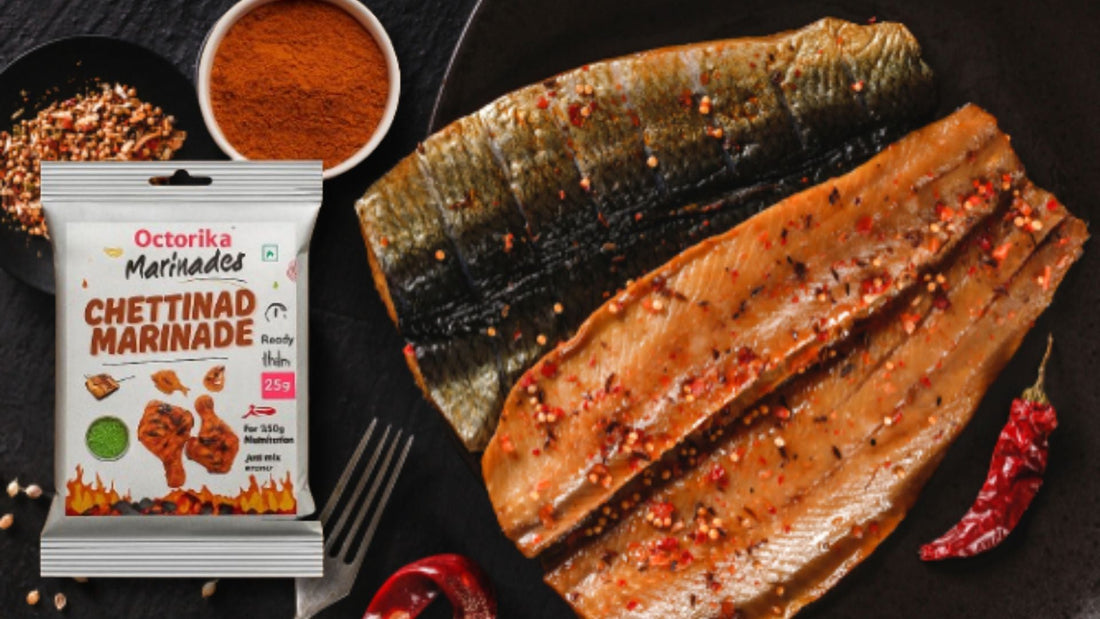 A close-up of raw fish fillets marinated with red spices and chili flakes, placed on a dark plate alongside a pack of Octorika Chettinad Marinade, with visible bowls of red chili powder and crushed spices in the background